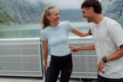 Two individuals wearing Odlo performance apparel outdoors by a mountain lake, highlighting clothing enhanced with HeiQ Mint technology for comfort during active lifestyles.