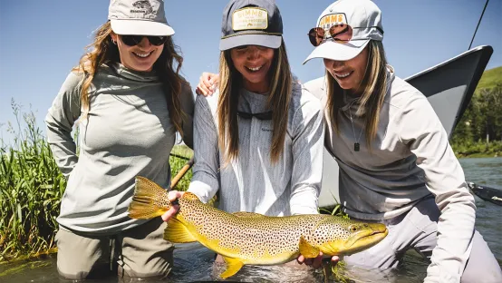 Three women holding a fish, wearing SIMMS shirts featuring HeiQ Fresh™ technology.